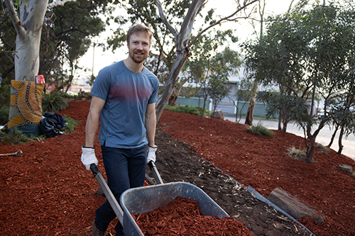 Man in a blue T-shirt smiling at the camera while pushing a trolley while gardening